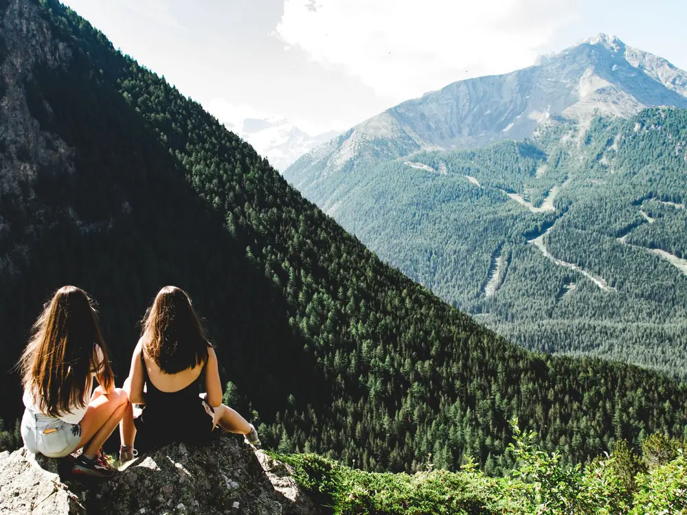 Two travellers sitting on a rock looking over an alpine valley