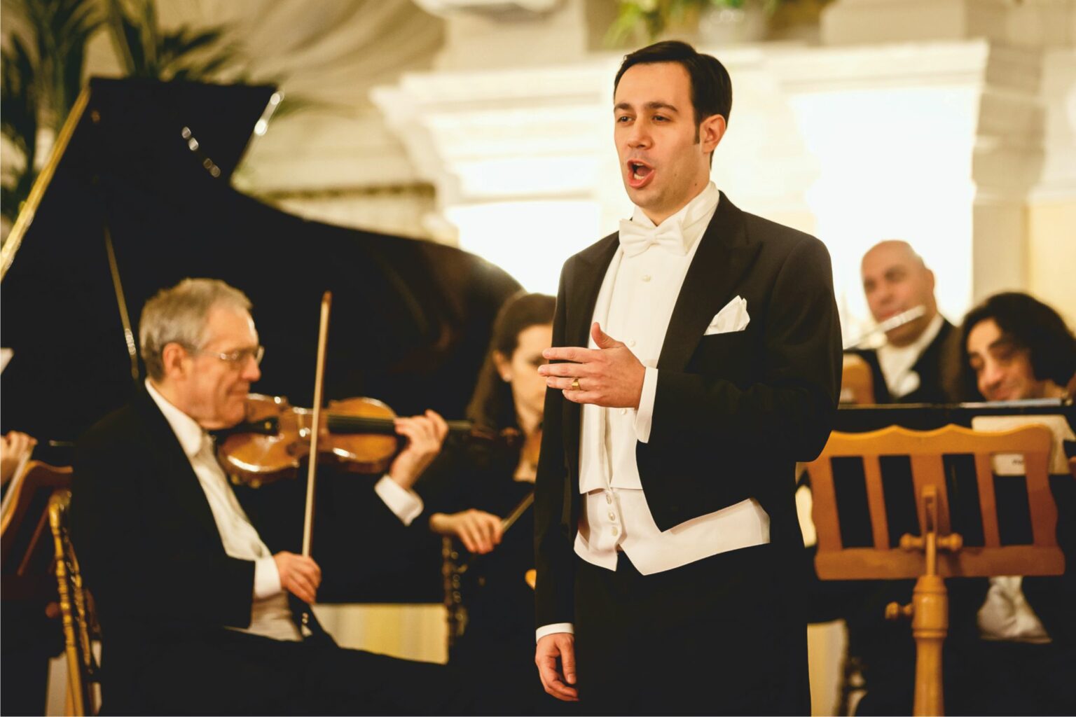 Mann singt bei einem klassischen Konzert mit Orchester im Hintergrund